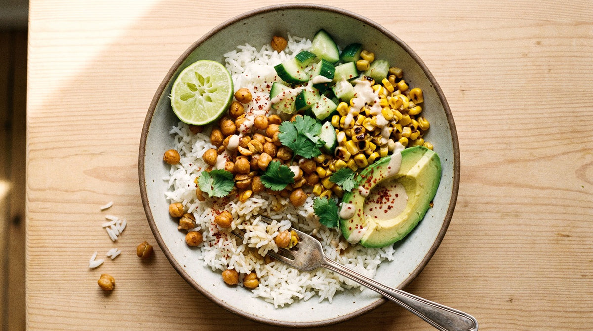 Rice bowl with crispy chickpeas seasoned with Chooki's Chilli Chicken Salt, charred corn, cucumber, avocado and lime tahini on a wooden table