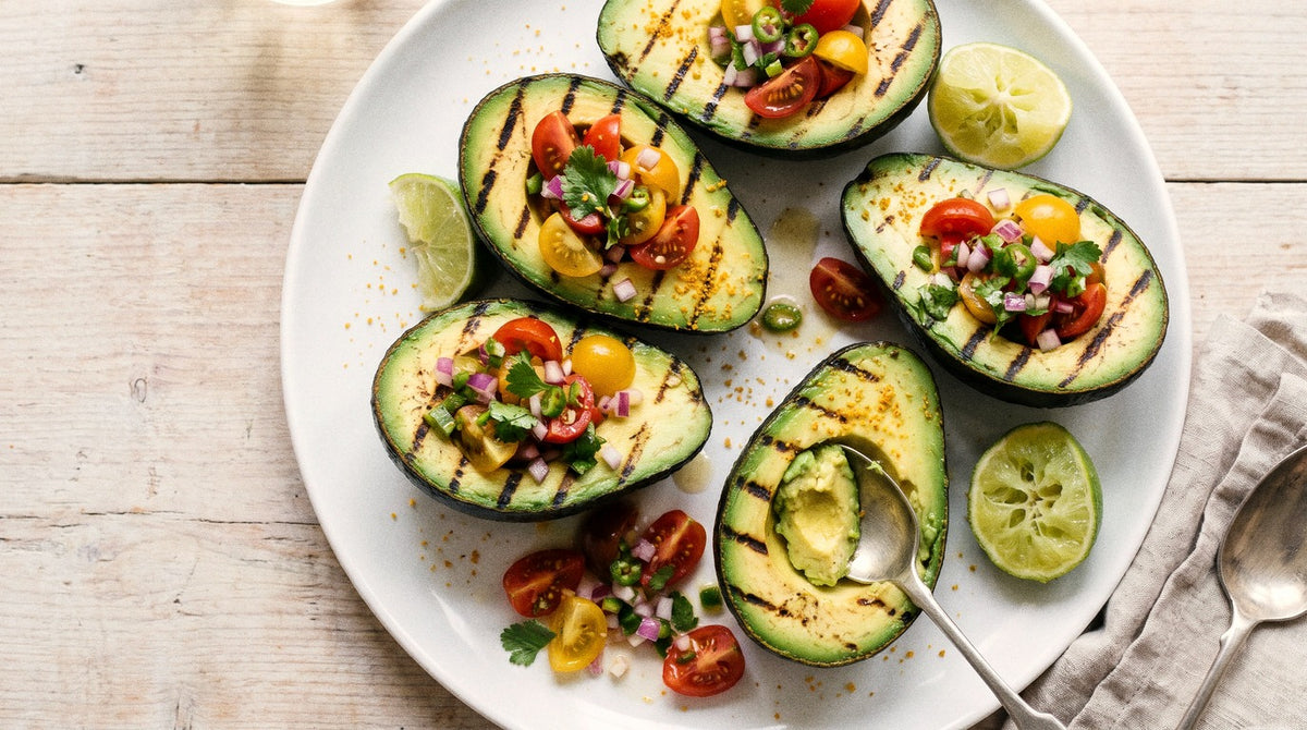 Chargrilled avocado halves filled with cherry tomato and lime salsa, seasoned with Chooki's Original Chicken Salt on a white plate