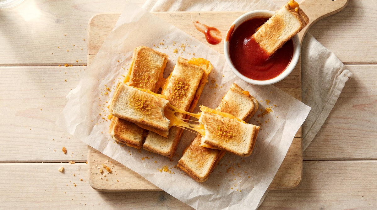 Cheese toastie soldiers seasoned with Chooki's Original Chicken Salt beside a bowl of tomato dip on a wooden board