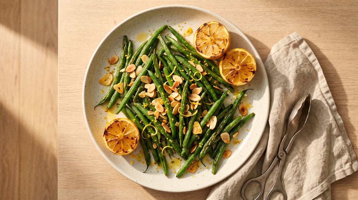 Blistered green beans with toasted flaked almonds, crispy garlic and lemon zest seasoned with Chooki's Vinegar Chicken Salt on a ceramic plate with charred lemon halves