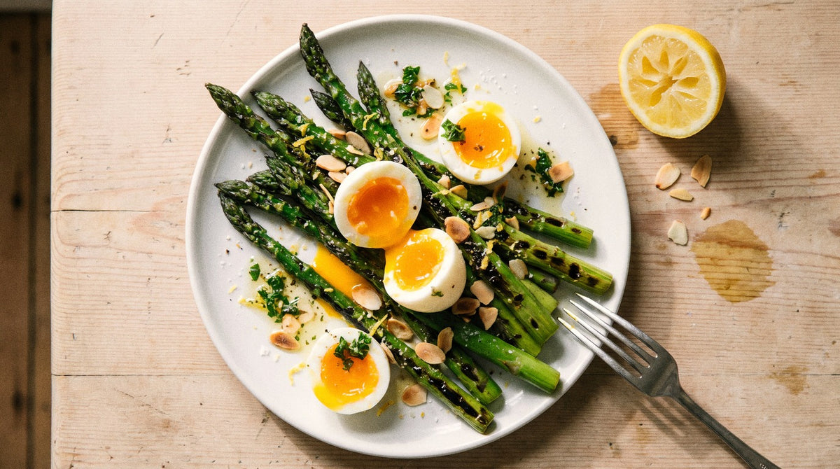 Charred asparagus with halved jammy eggs, lemon herb oil and toasted almonds seasoned with Chooki's Zest Chicken Salt on a white plate
