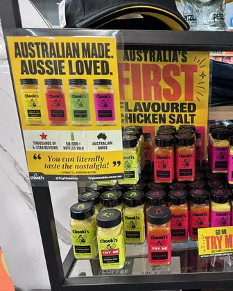A tall stack of Chooki's chicken salt jars under the Australia's first flavoured chicken salt poster at Ceduna Camping and Fishing